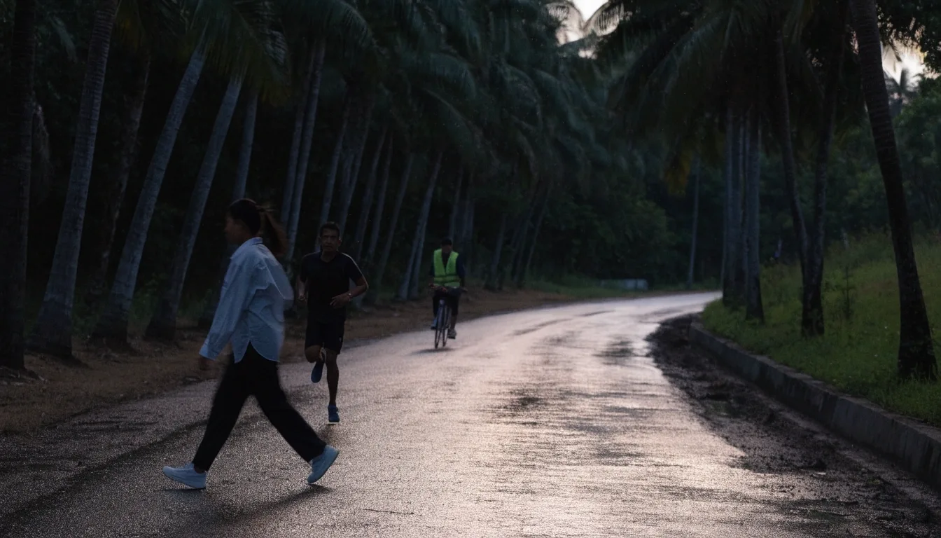 Pengguna jalan kaki, pelari pagi, dan pesepeda melewati jalur tepi jalan berlampu rendah saat fajar